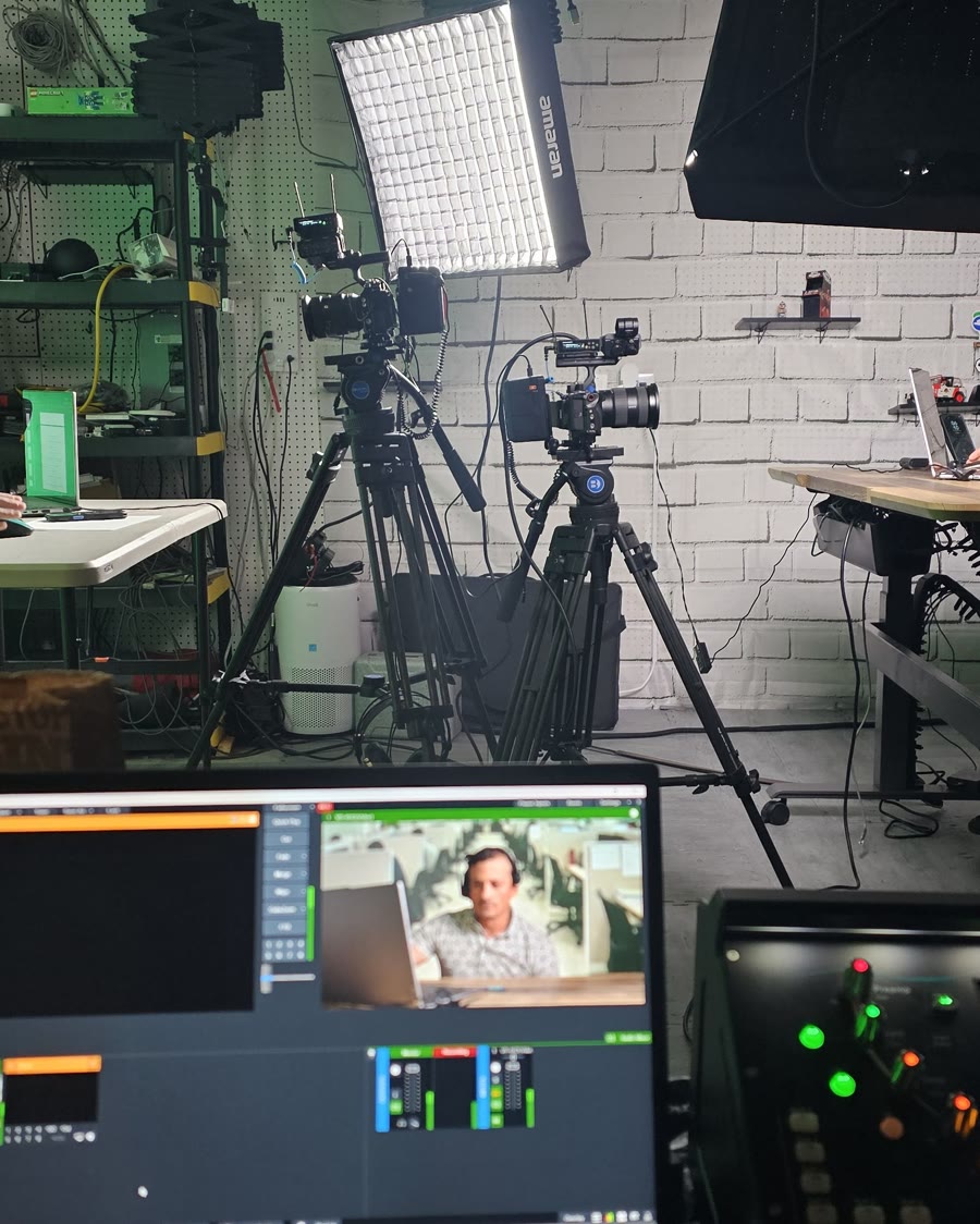 Two cameras on tripods beside a soft light in The Studio Creative's studio, with an audio mixer and a monitor in the foreground