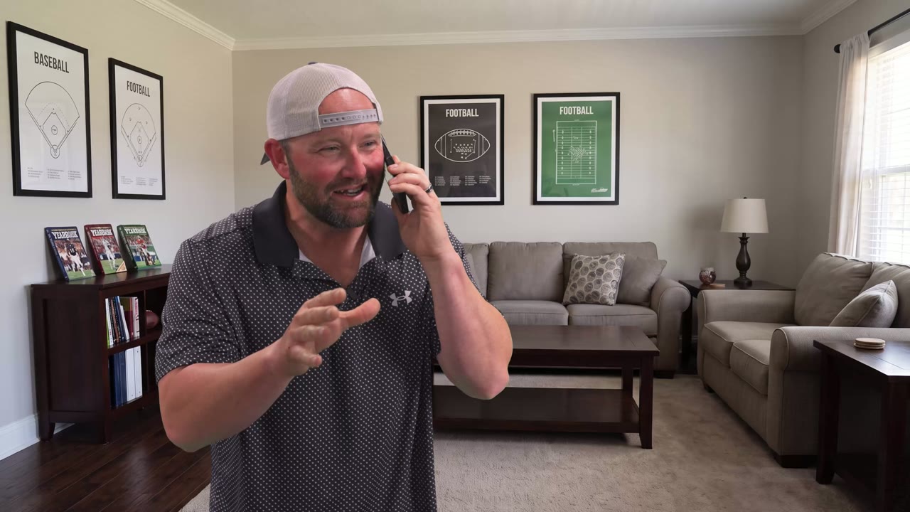 A man in a backwards cap and polo on his phone in a virtual living room with football prints on the wall