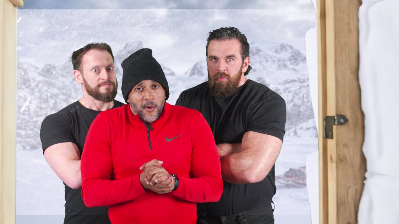 Three men in a snowy doorway, one in a red top and black beanie between two bodyguards, mountains and snow behind them