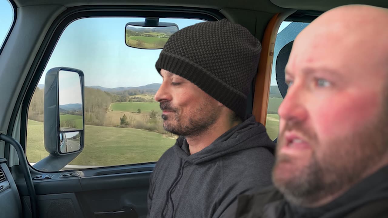 Two men riding in the cab of a truck with rolling countryside through the windows