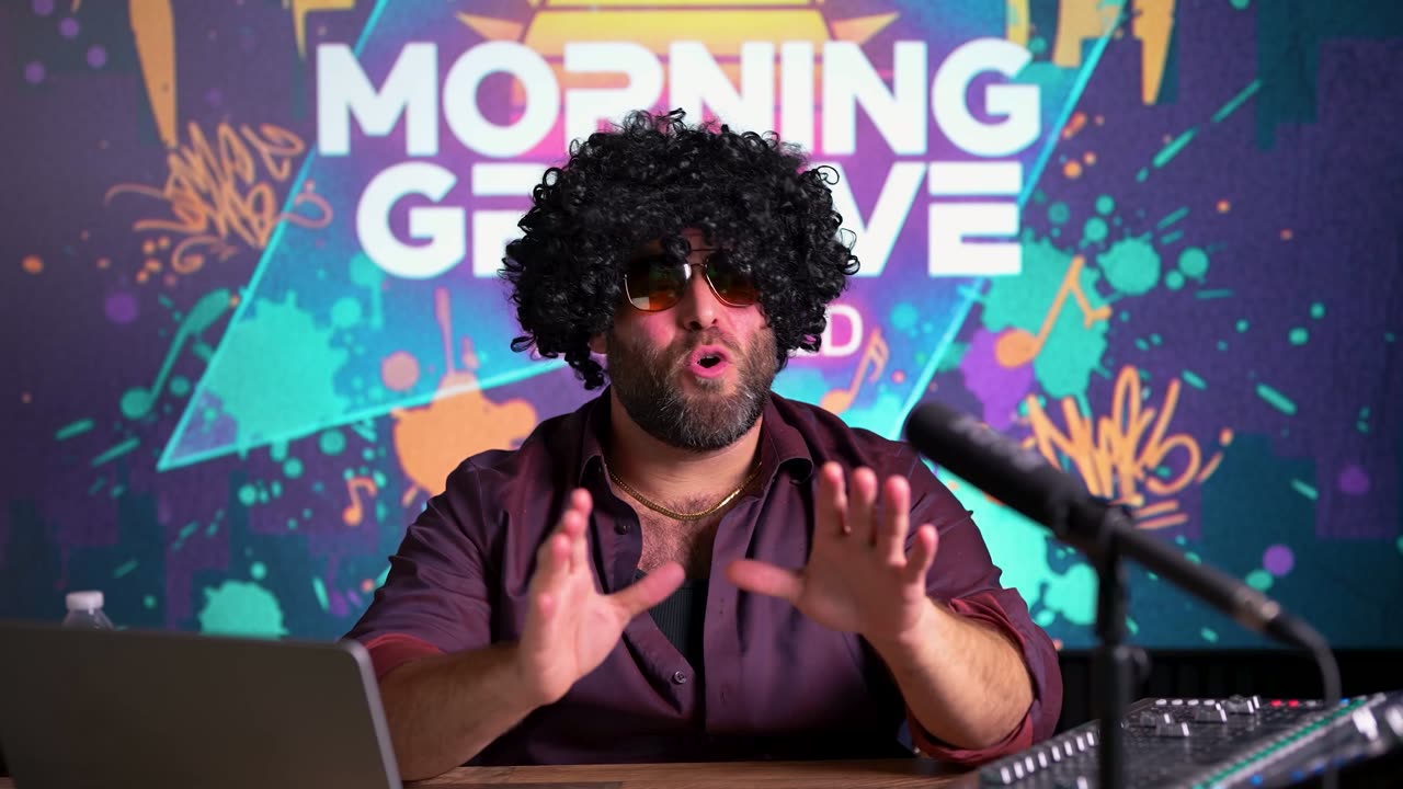 A radio host in an afro wig and sunglasses at a microphone in front of a Morning Groove sign