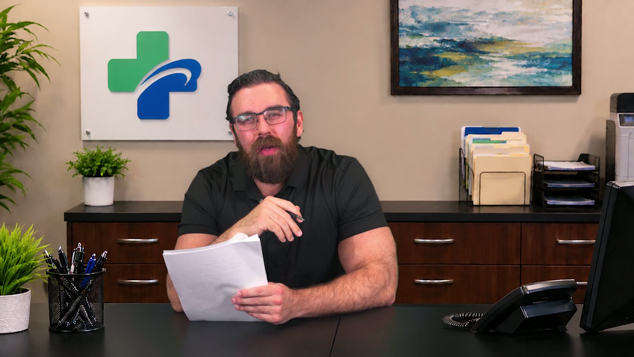 Receptionist in glasses reading paperwork at the front desk of a clinic set with a green cross logo