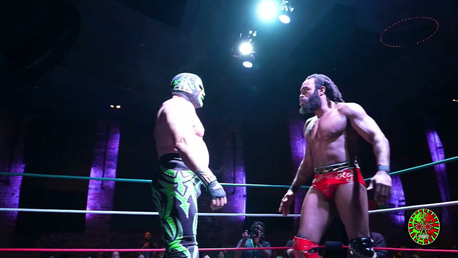 Two wrestlers facing off in the ring at Lucha Boom, brightly lit from above with the crowd darker behind them