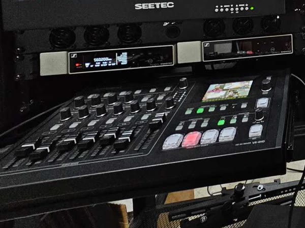 A Roland VR-4HD switcher and rack-mounted Sennheiser wireless receivers under a multiview monitor at The Studio Creative